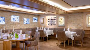 A restaurant with wooden walls, stone accents, and a wine display. Tables are set with white tablecloths and brown chairs.