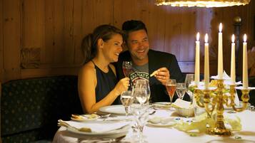 A couple dining at a table with candles and a candelabra, in a room with wooden walls and a patterned chair.