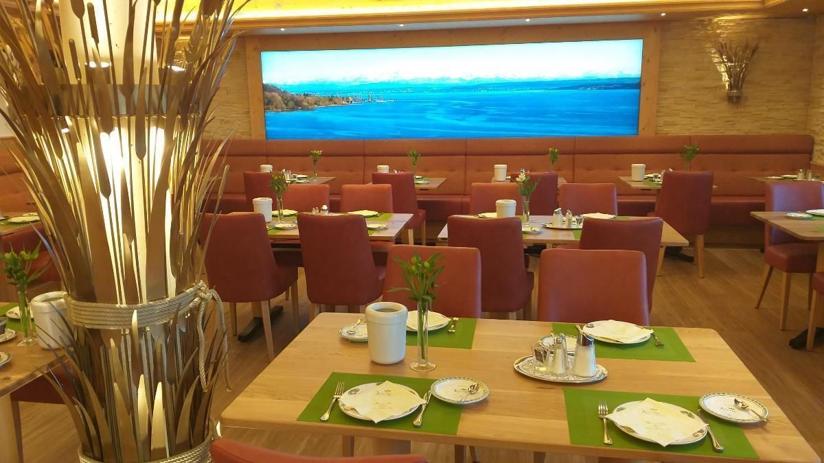 Una sala ristorante con tavoli apparecchiati, un grande schermo che mostra un panorama e una scultura decorativa in metallo.