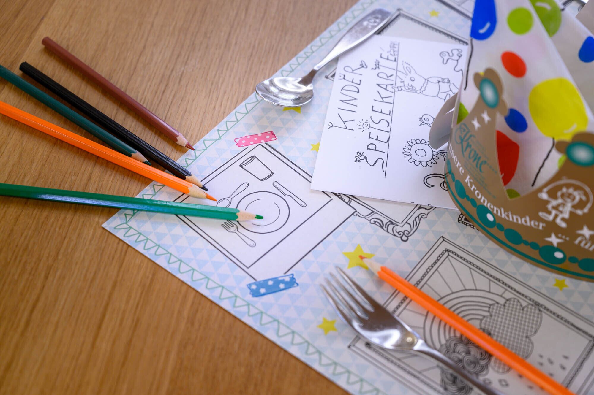 Une table avec un œuf Kinder Surprise, des crayons de couleur et une cuillère, le tout posé sur une nappe à motifs.