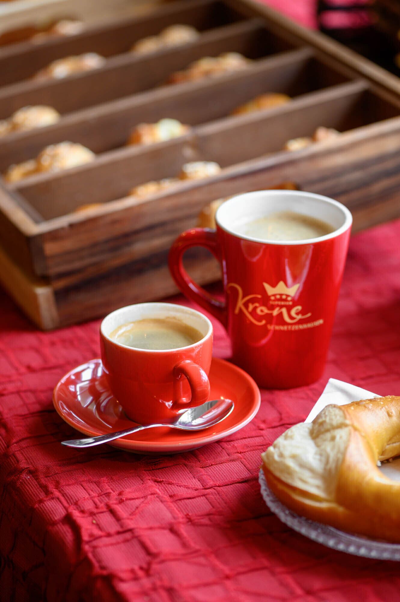Una bandeja de pasteles, una taza de café y una dona sobre un mantel rojo.