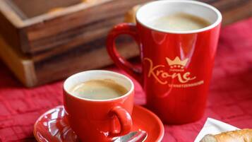 Una bandeja de pasteles, una taza de café y una dona sobre un mantel rojo.