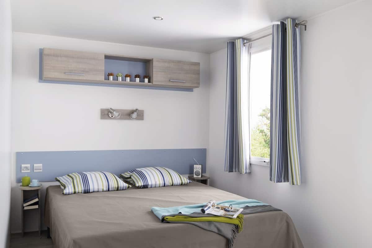 Ein Schlafzimmer mit einem Bett, einem Nachttisch, einer Ablage mit Dekoration, einem Fenster mit Vorhängen und einem grünen Teppich.