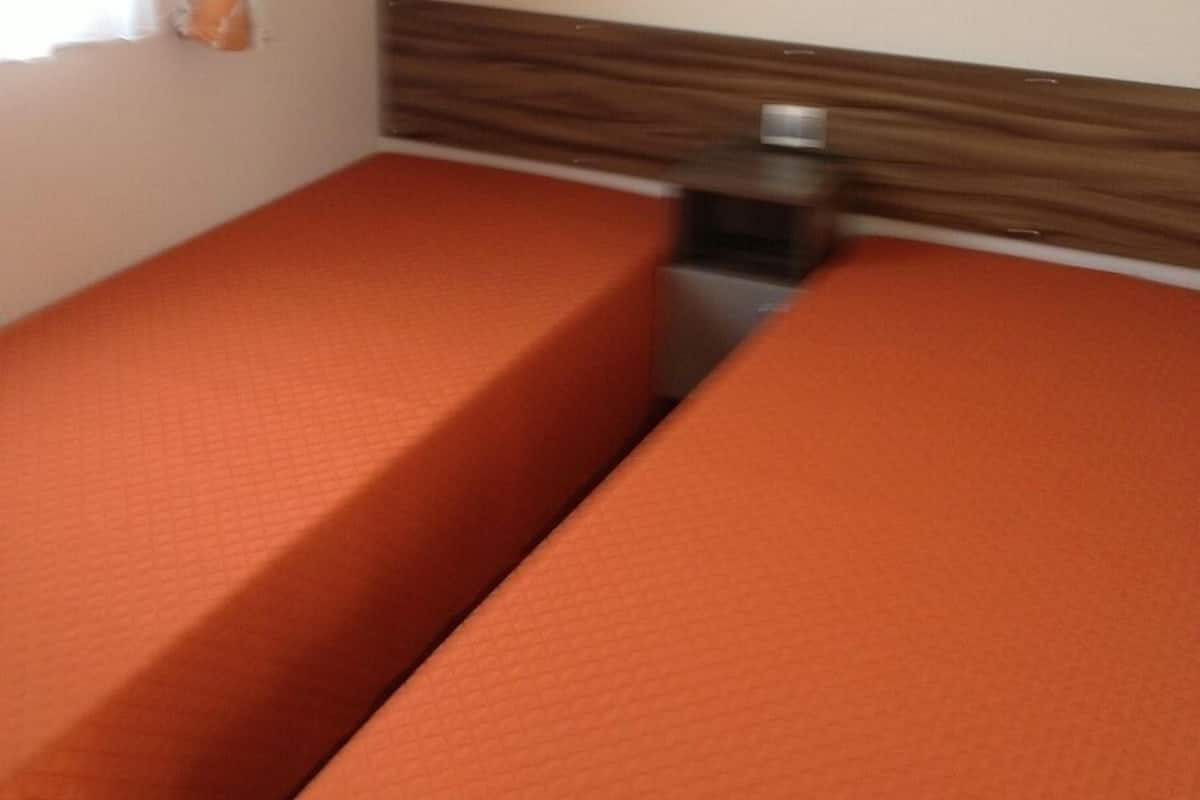 Ein Zimmer mit zwei Betten, einem Holzkopfende, einem kleinen Tisch und einem Spiegel an der Wand.