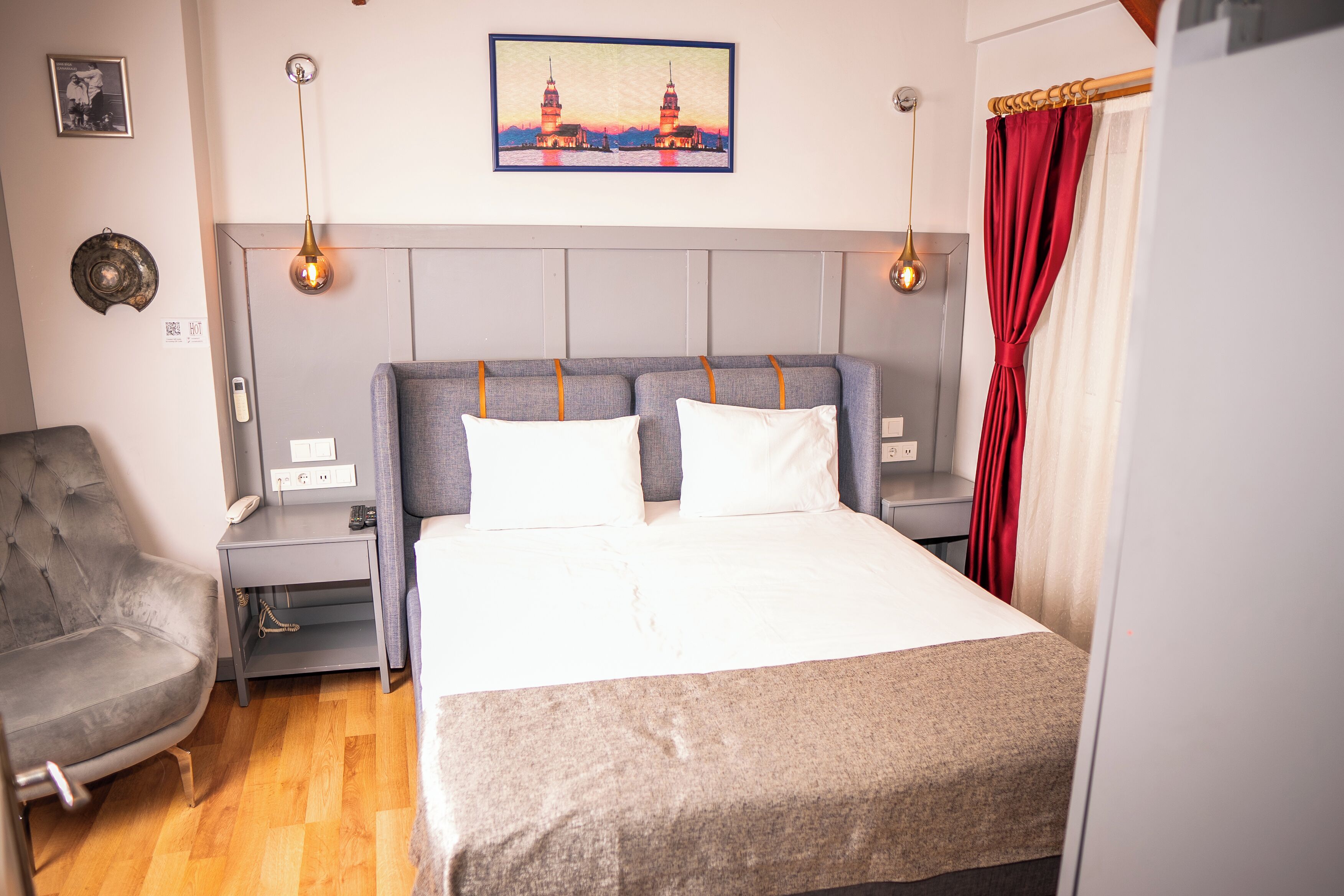 Quarto de hotel com cama, cadeira, mesa de cabeceira, luminária na parede e quadro sobre a cama.