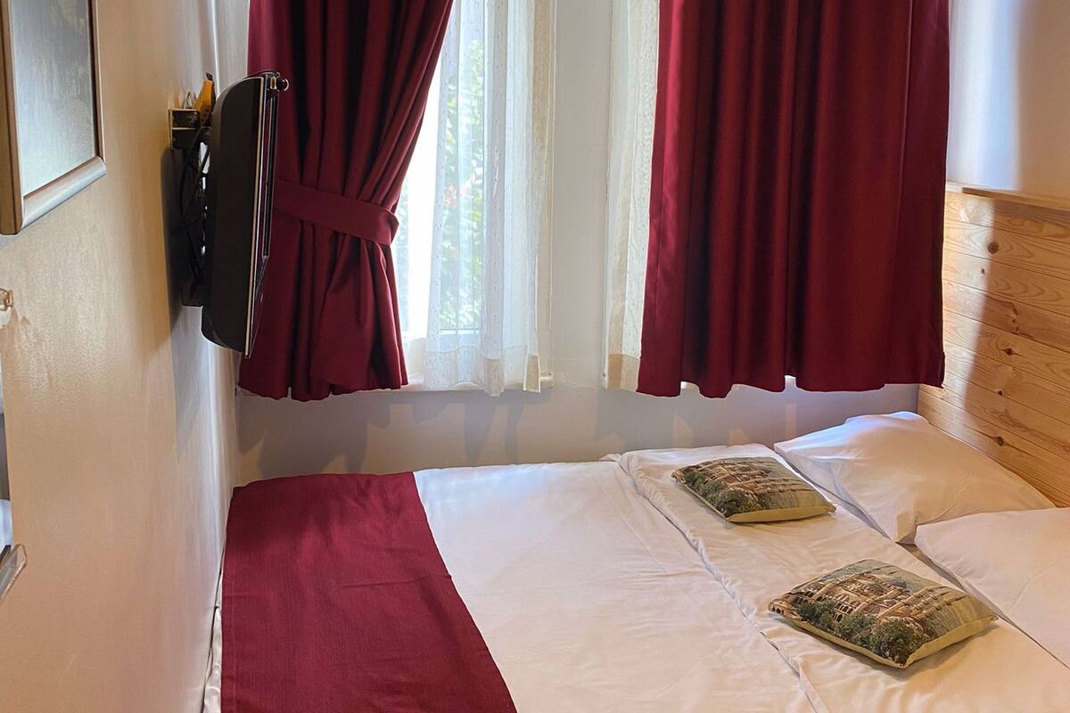 Un dormitorio con cama, cortinas rojas, una araña y un cabecero de madera.