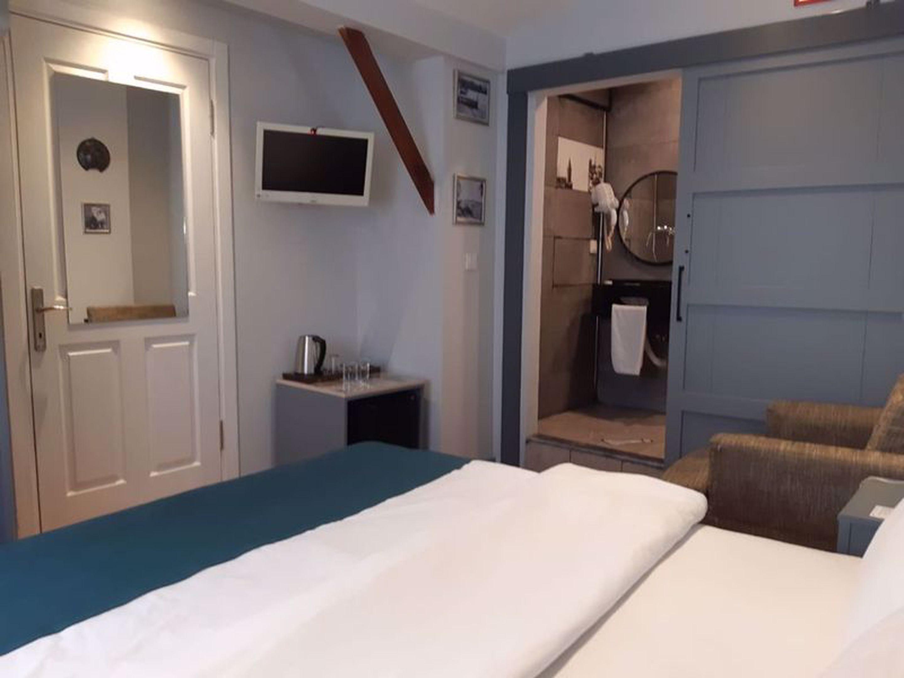 A hotel room with a bed, a desk, a TV, a shower area, and a bathroom.