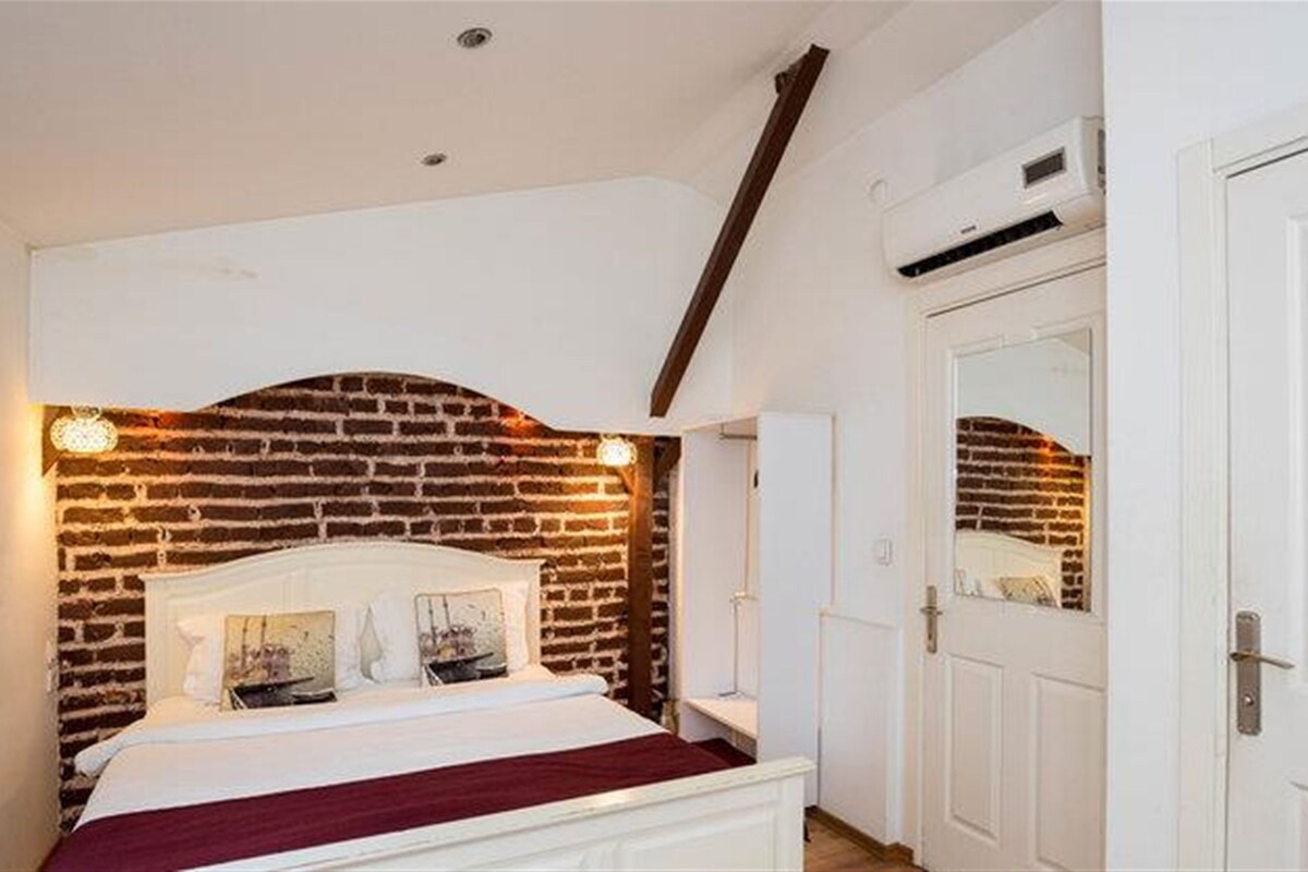 A bedroom with a brick-patterned headboard, a white bed, and a white door with a mirror.