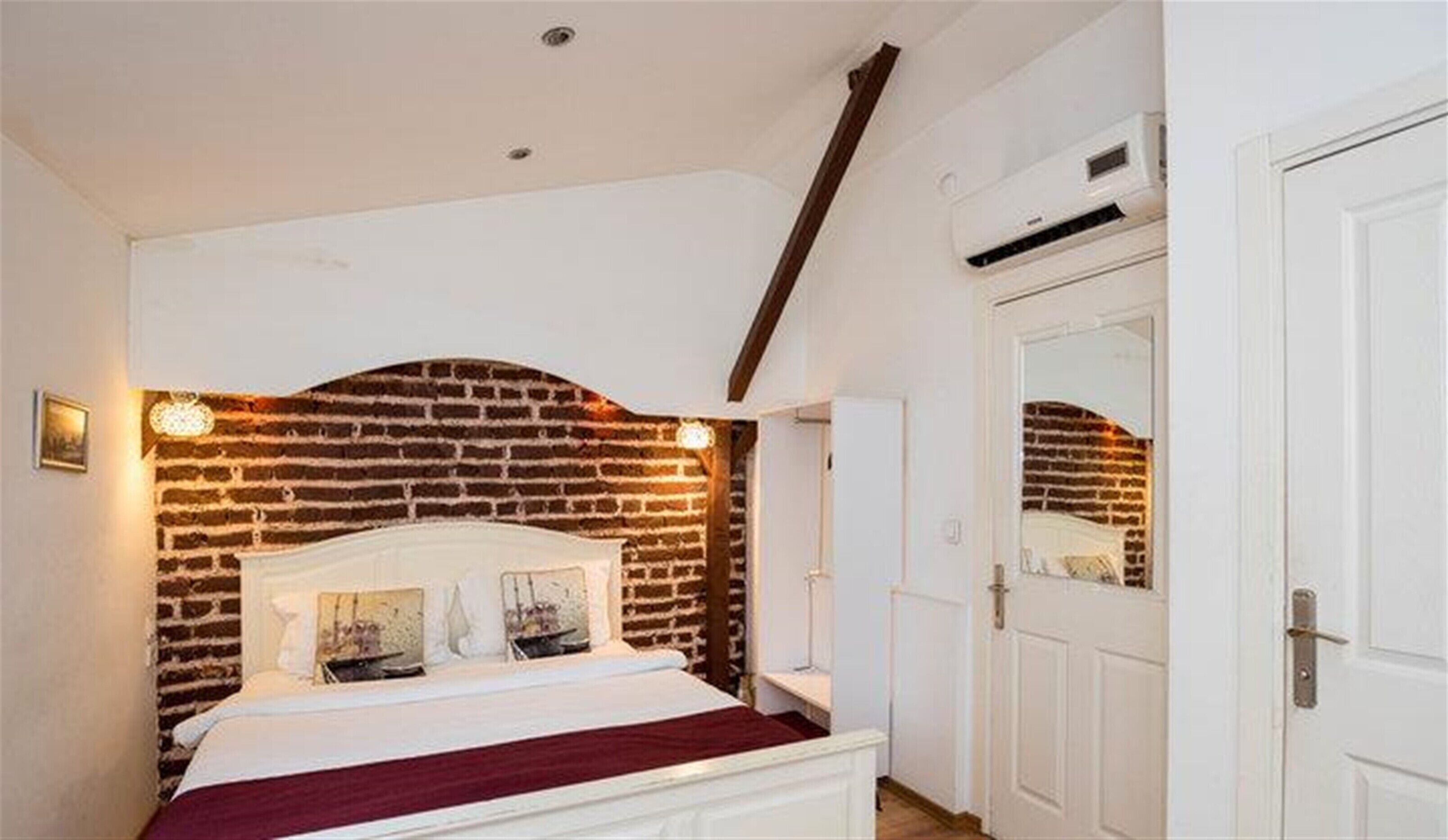 A bedroom with a brick-patterned headboard, a white bed, and a white door with a mirror.