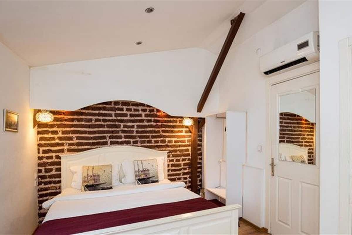 Un dormitorio con cabecera de ladrillo, cama blanca y puerta blanca con espejo.