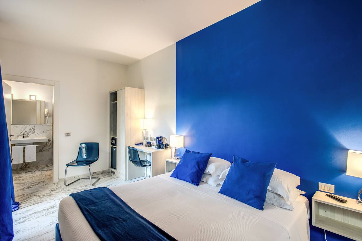 A hotel room with a large bed, a desk, a chair, and a bathroom visible through an open door.