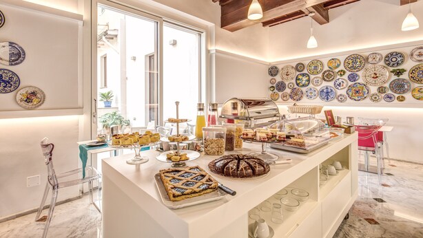 Un bufé de desayuno con diversos pasteles y postres, una estación de café y una pared decorada con platos de colores.