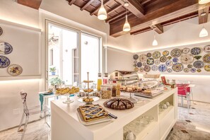 Un buffet de petit-déjeuner proposant une variété de viennoiseries et de desserts, un coin café et un mur décoré d’assiettes colorées.