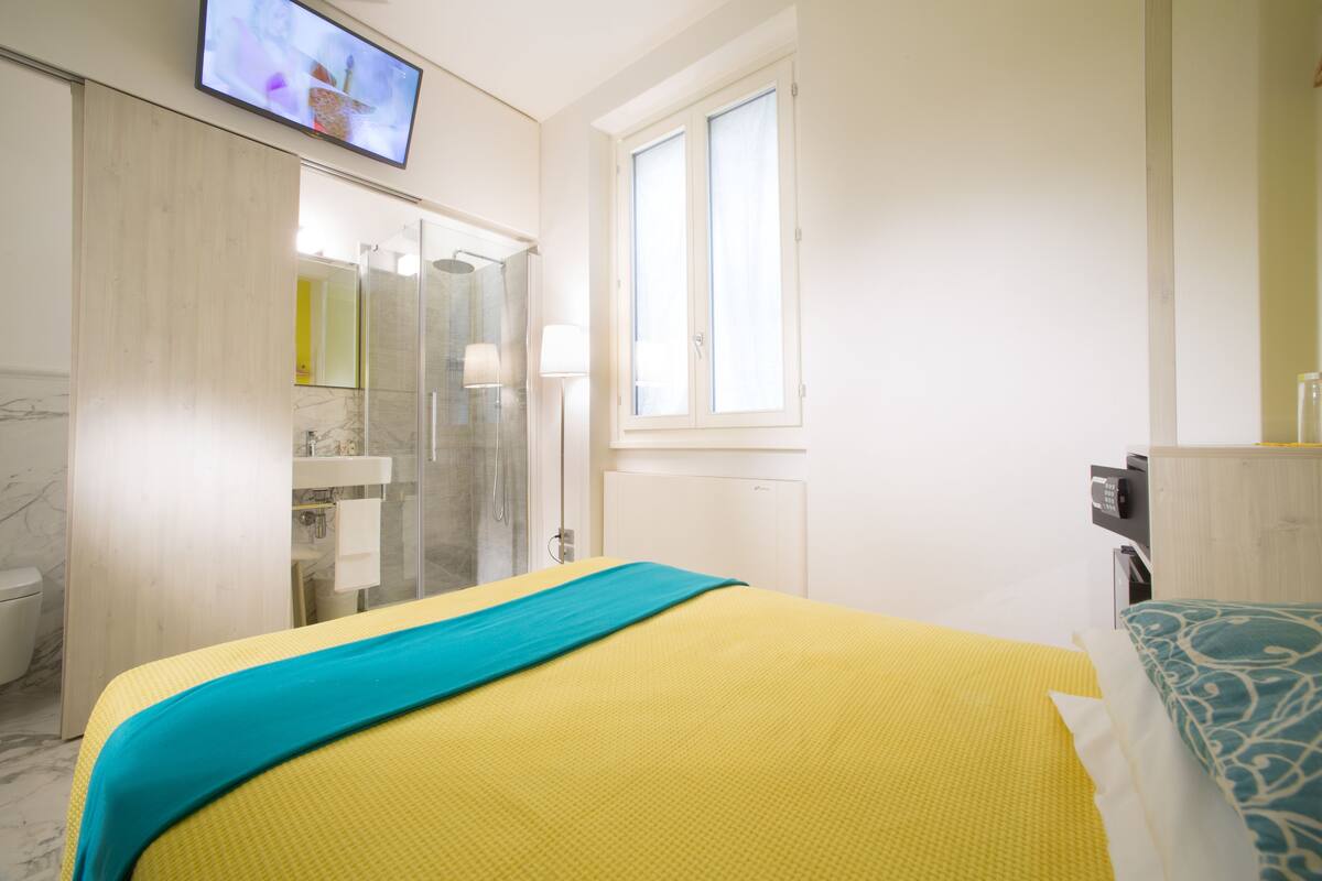 A hotel room with a bed, a bathroom, a TV, and a window.