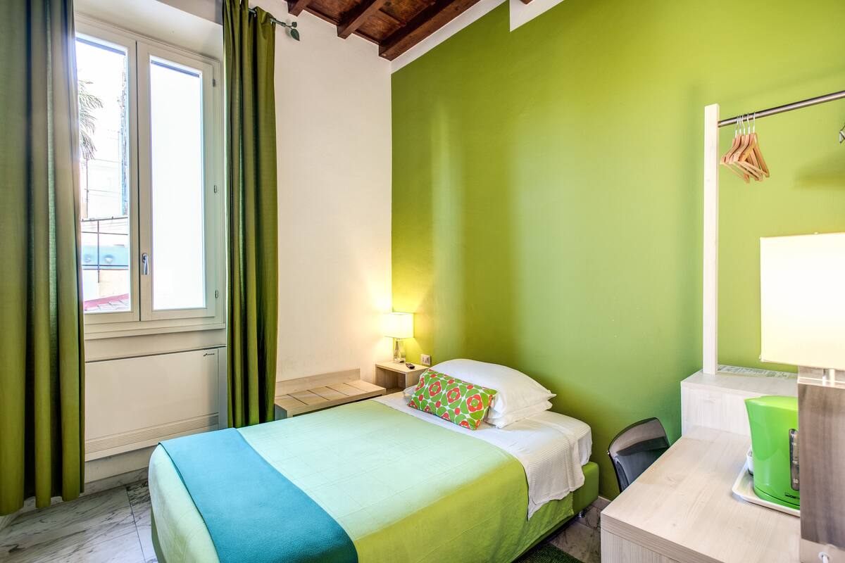 A hotel room with a bed, a nightstand, a chair, a desk, and a window with curtains.