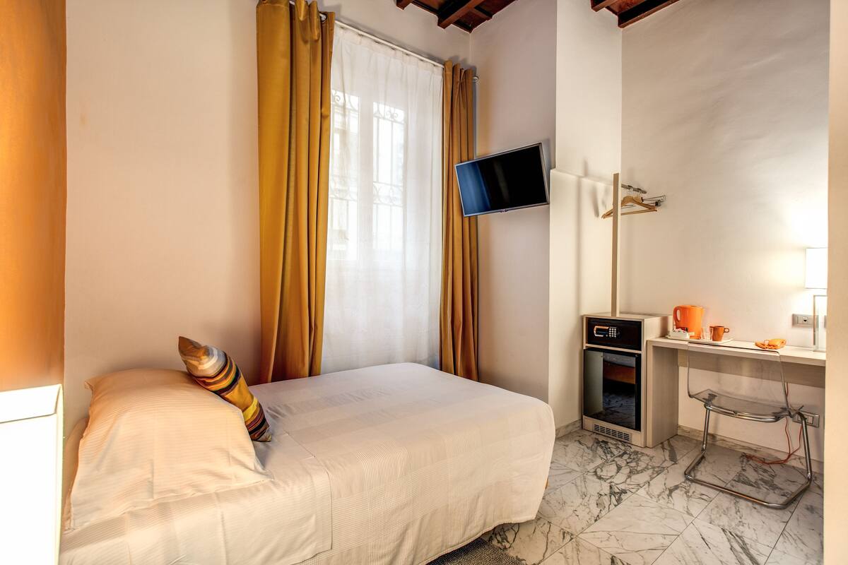 A hotel room with a bed, a TV mounted on the wall, a desk with a microwave, and a coffee maker.