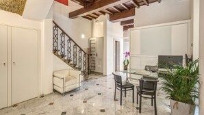 Un espacio habitable amplio con piso de mármol, un sofá blanco, una mesa de comedor con sillas y una escalera con barandales ornamentados.