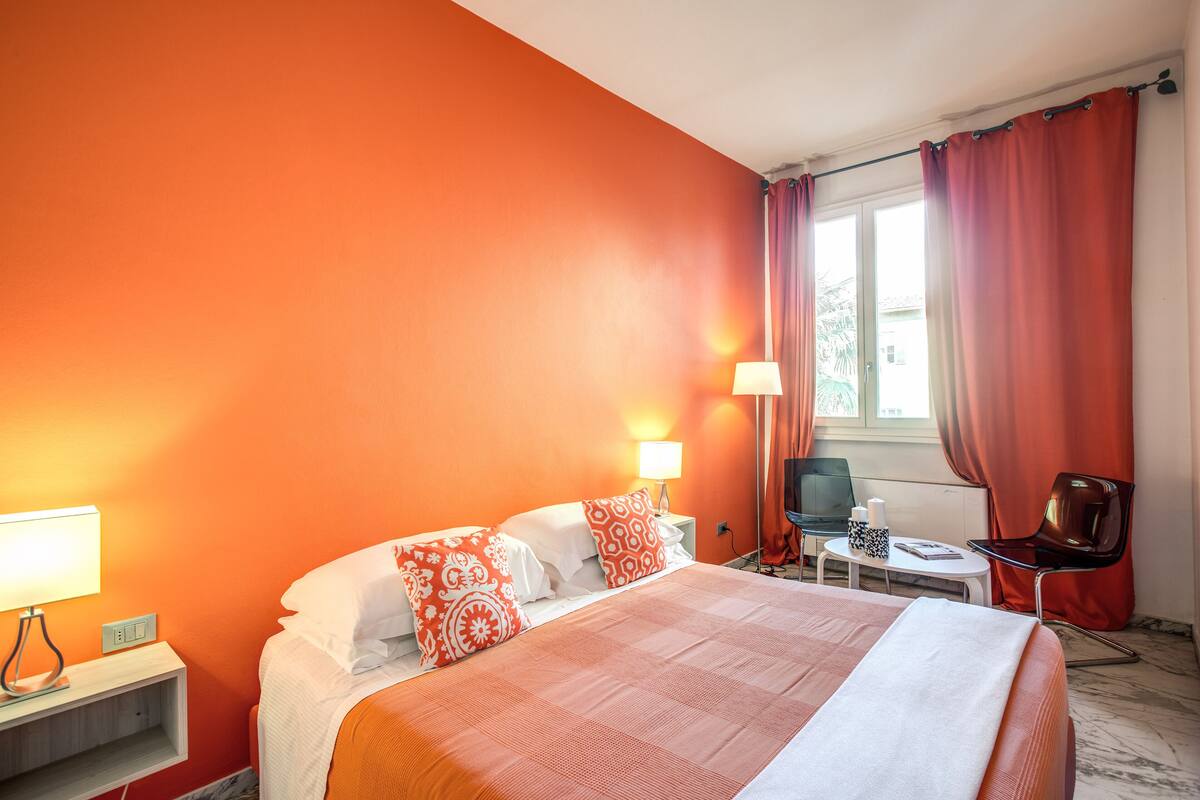 A hotel room with a large bed, two bedside lamps, a desk with a chair, and a window with curtains.
