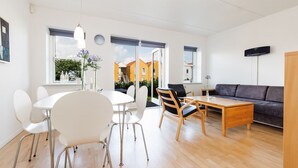 A modern living room with a dining area, a sofa, and a TV. There are large windows with a view of buildings outside. - Hotel Rudkøbing Skudehavn (Rudkobing)