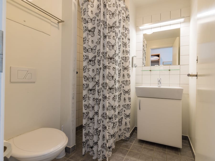 Un baño con inodoro, lavamanos y cortina de ducha con estampado de mariposas.