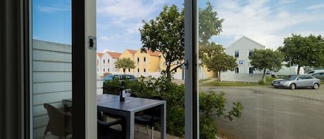 A view from a window with a table and chairs outside, a parking sign, and buildings in the background.