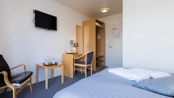 A hotel room with a bed, a desk with a chair, a TV mounted on the wall, and a wardrobe.