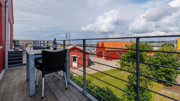 A balcony with a table and chairs, overlooking a marina with boats and a red building labeled "NEPTUN." - Hotel Rudkøbing Skudehavn (Rudkobing)