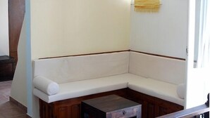 A corner sofa with a wooden base, a small wooden table with a drawer, and a decorative plate on the wall. - Akti Rooms (Astypalaia)