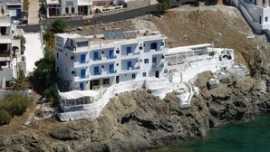 A multi-story building with balconies, situated on a rocky coastline. - Akti Rooms (Astypalaia)