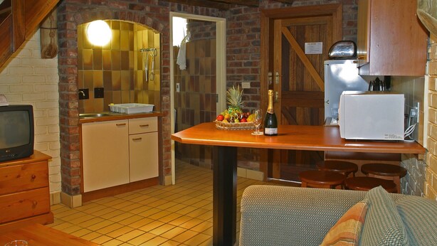 Una cocina acogedora con pared de ladrillo, armarios de madera, piso de baldosas, un rincón de comedor pequeño y un televisor.