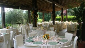 An outdoor covered dining area with round tables set for a formal event, surrounded by white chairs and covered with tablecloths. - Fattoria Il Santo (Monticiano)