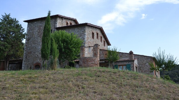 Un bâtiment en pierre doté d’une tour, entouré d’arbres et bordé d’un terrain herbeux.