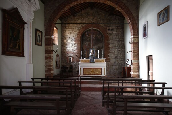 An interior of a church with wooden pews, a central altar, and a stone wall with a cross.