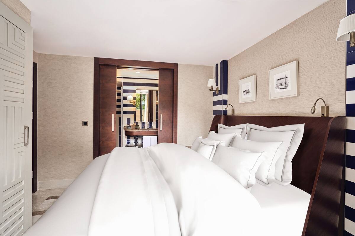 Une chambre d’hôtel avec un grand lit, une tête de lit en bois, une salle de bain avec un miroir et des tableaux encadrés accrochés au mur.