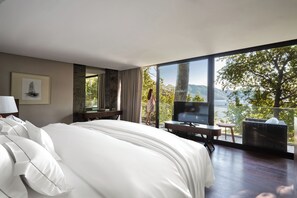 A modern hotel room with a large bed, a TV, and a balcony with a view of the mountains.