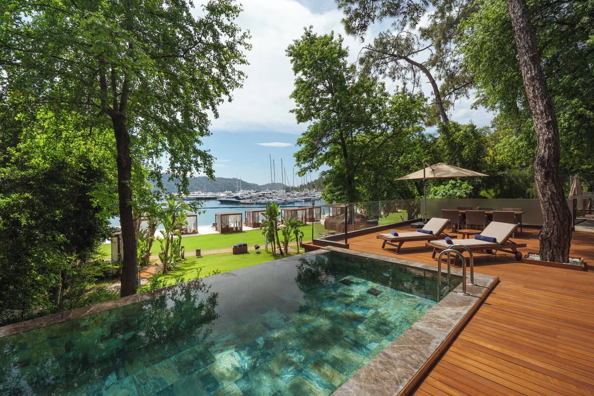 Un espace piscine doté d’une terrasse en bois, de chaises longues et offrant une vue sur les bateaux et les collines.