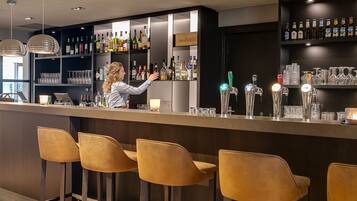 Uma área de bar com um bartender, banquetas, prateleiras cheias de garrafas de bebidas e utensílios de bar.