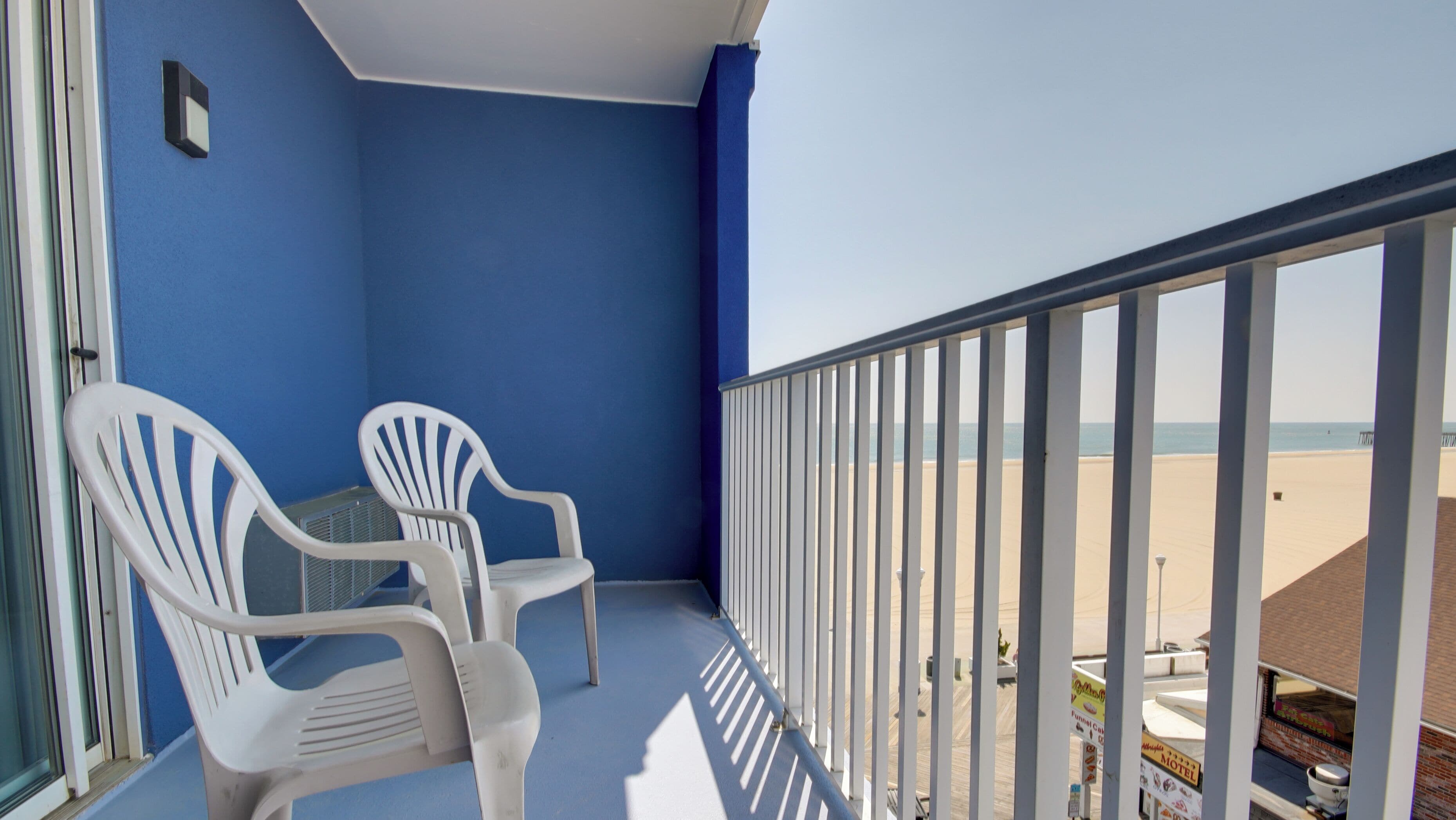 Un balcon avec deux chaises en plastique blanches, un mur bleu et une vue sur la plage.