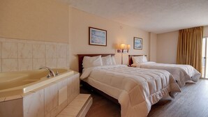 Habitación de hotel con una bañera grande, dos camas con ropa blanca, un cabecero de madera y un cuadro en la pared.