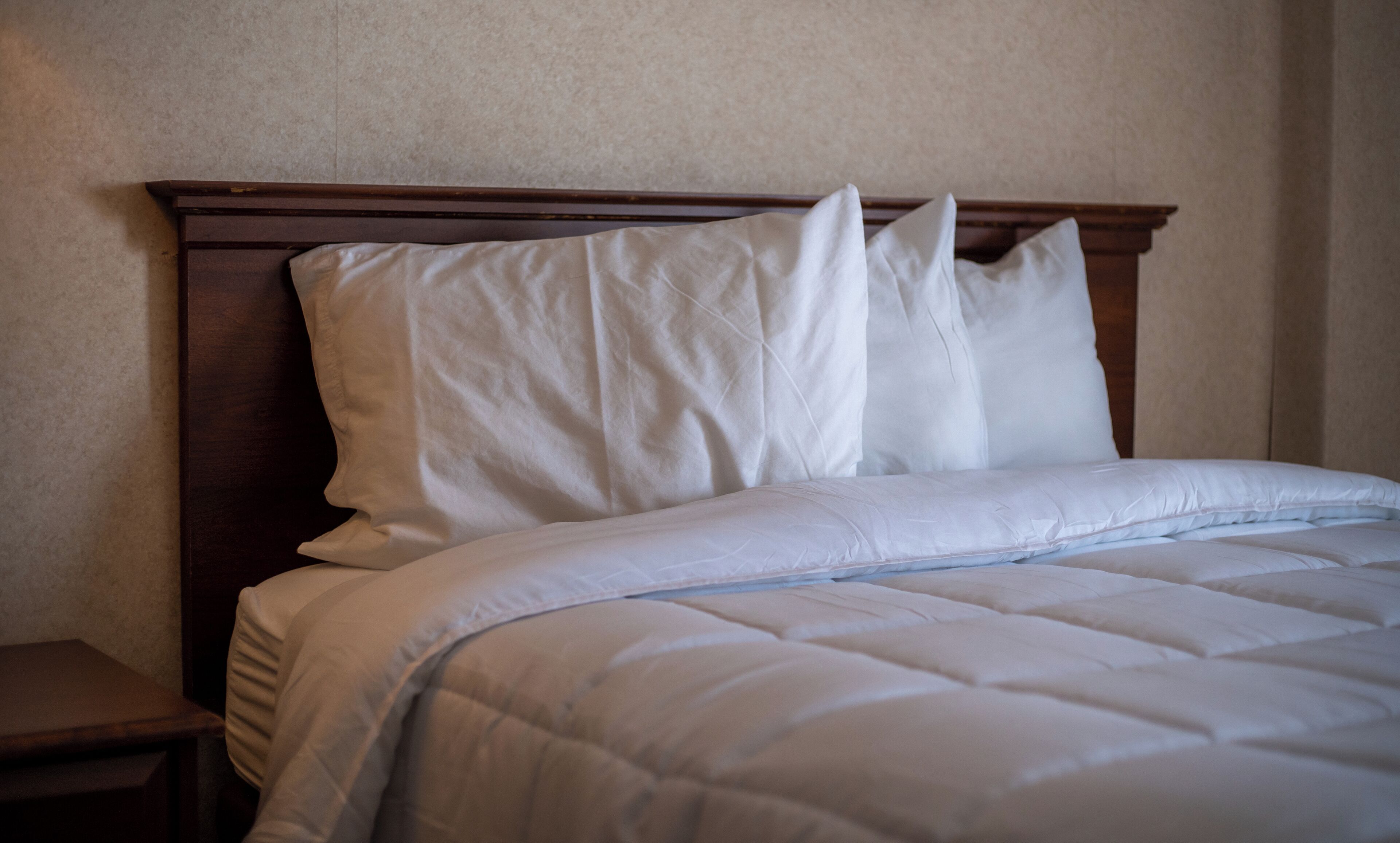 Una cama bien hecha con ropa blanca y un cabecero de madera.
