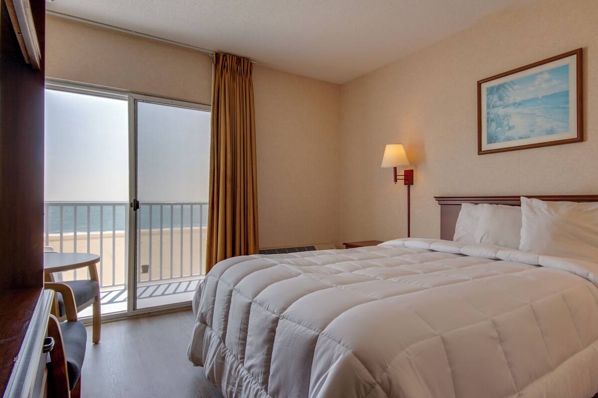Una habitación de hotel con cama, escritorio, silla, lámpara y un cuadro en la pared.