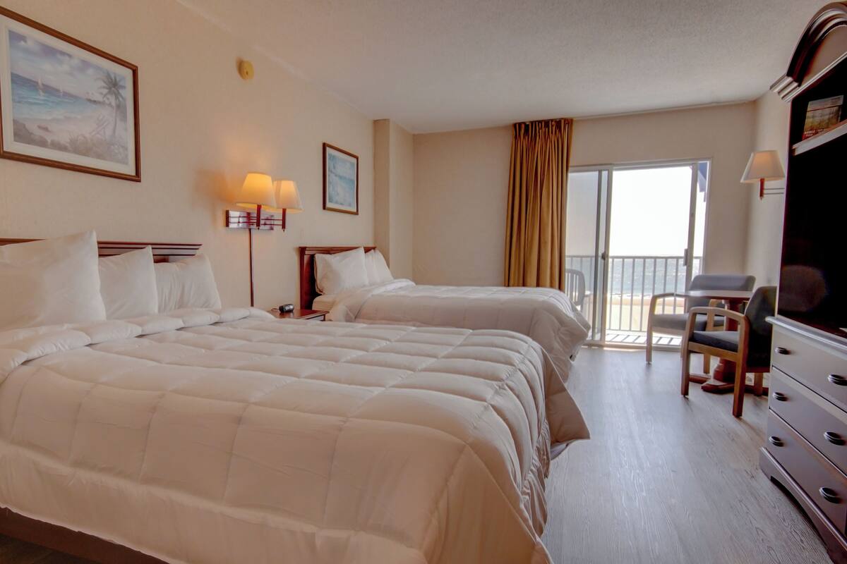Habitación de hotel con dos camas, televisión, escritorio y balcón con vistas.