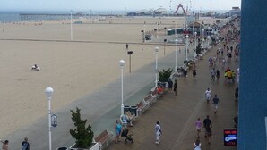 Un paseo marítimo con bancos y faroles que conduce a una playa y una noria a lo lejos.