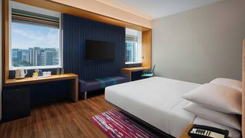 Una habitación de hotel moderna con una cama grande, un televisor montado en la pared, un escritorio con una silla y vistas de la ciudad a través de amplias ventanas.
