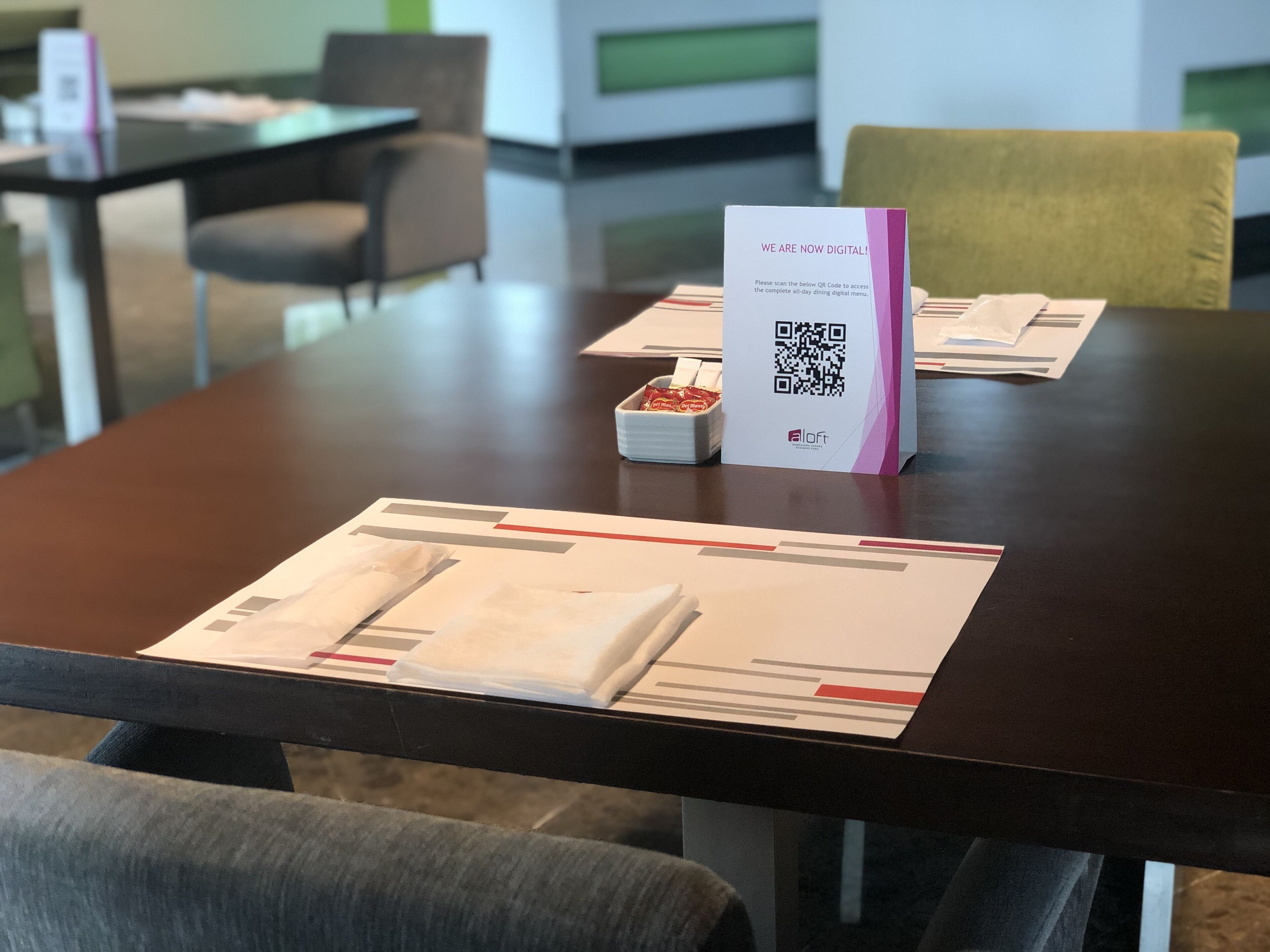 Et konferencelokal med et bord, en QR-kode til digital menukort, en lille snackæske og et kort med en QR-kode.