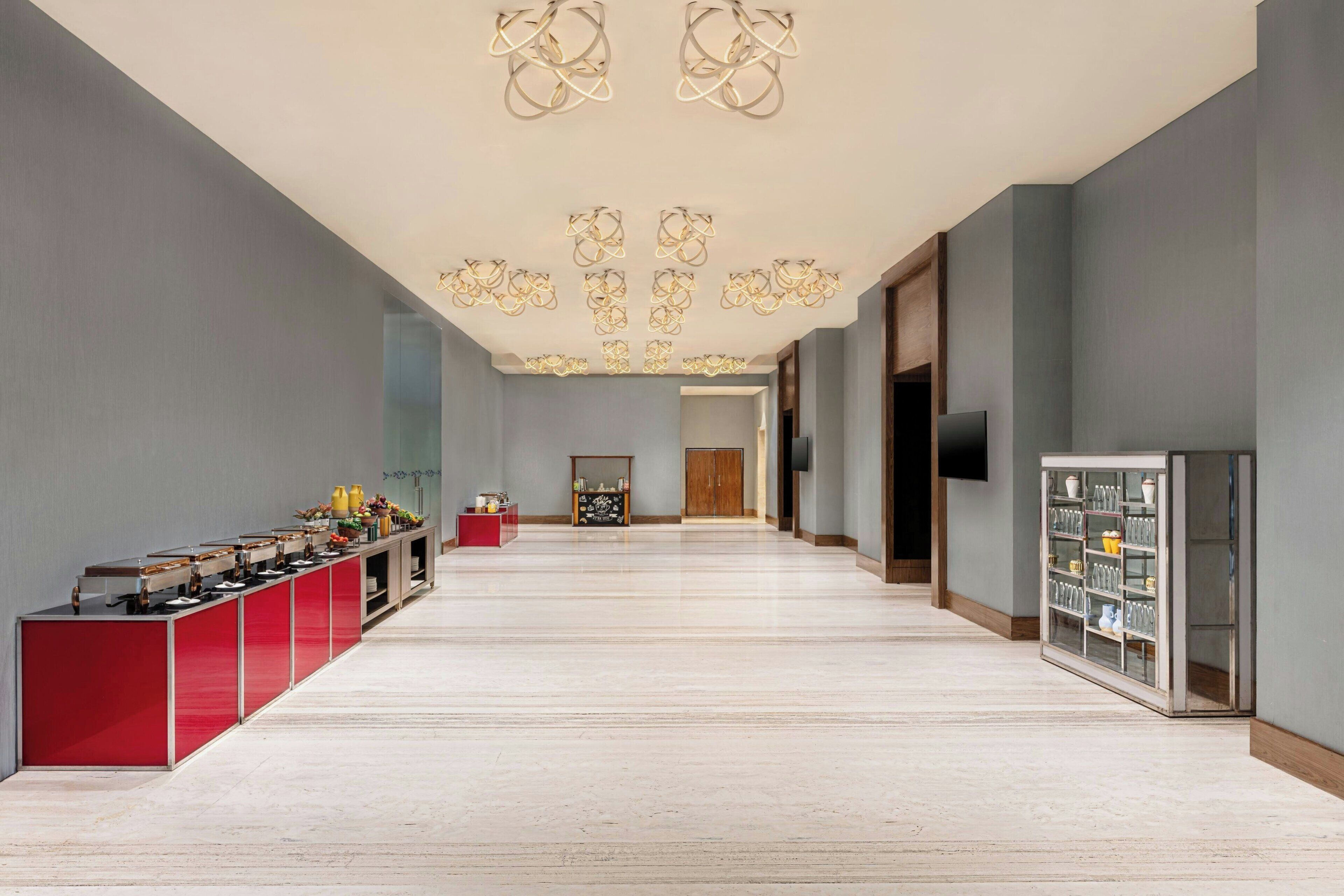 Corridoio di un hotel con un bancone di servizio rosso, una vetrina in vetro e un lampadario moderno.