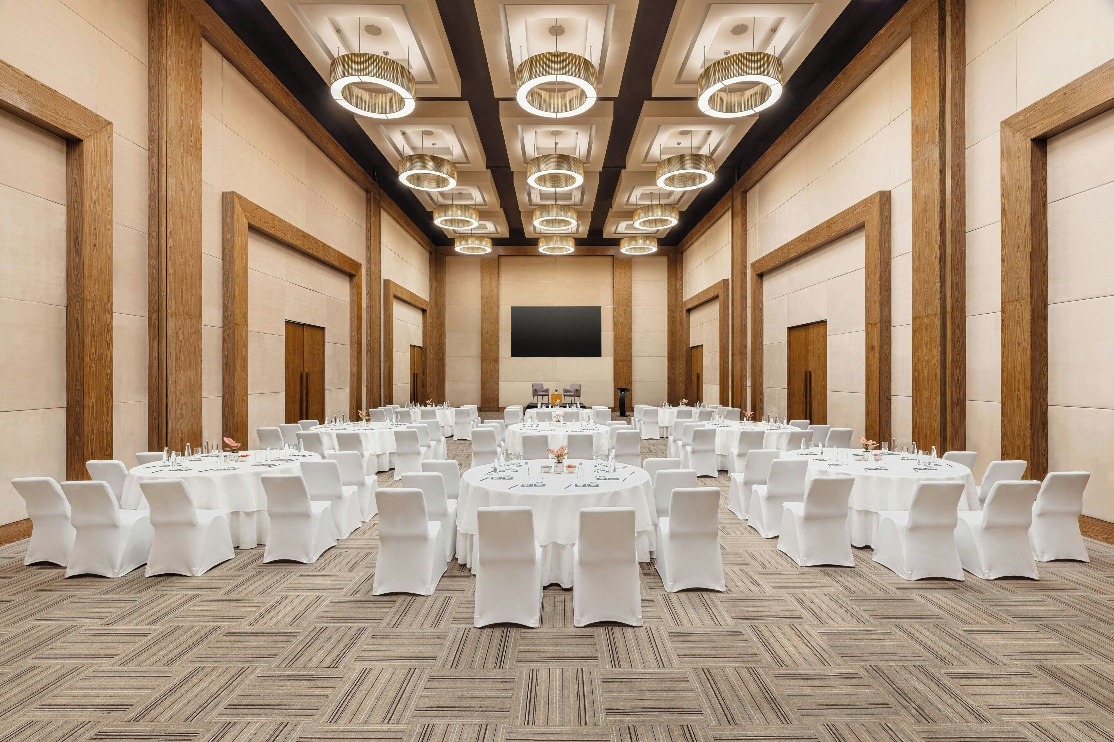 Uma grande sala de conferências com várias mesas redondas, cadeiras brancas e um design moderno no teto.