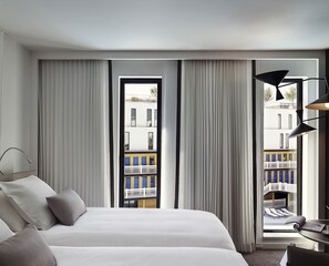A hotel room with a large bed, a desk, and a view of a building with balconies. - Molitor Hotel & Spa Paris - MGallery Collection (Paris)