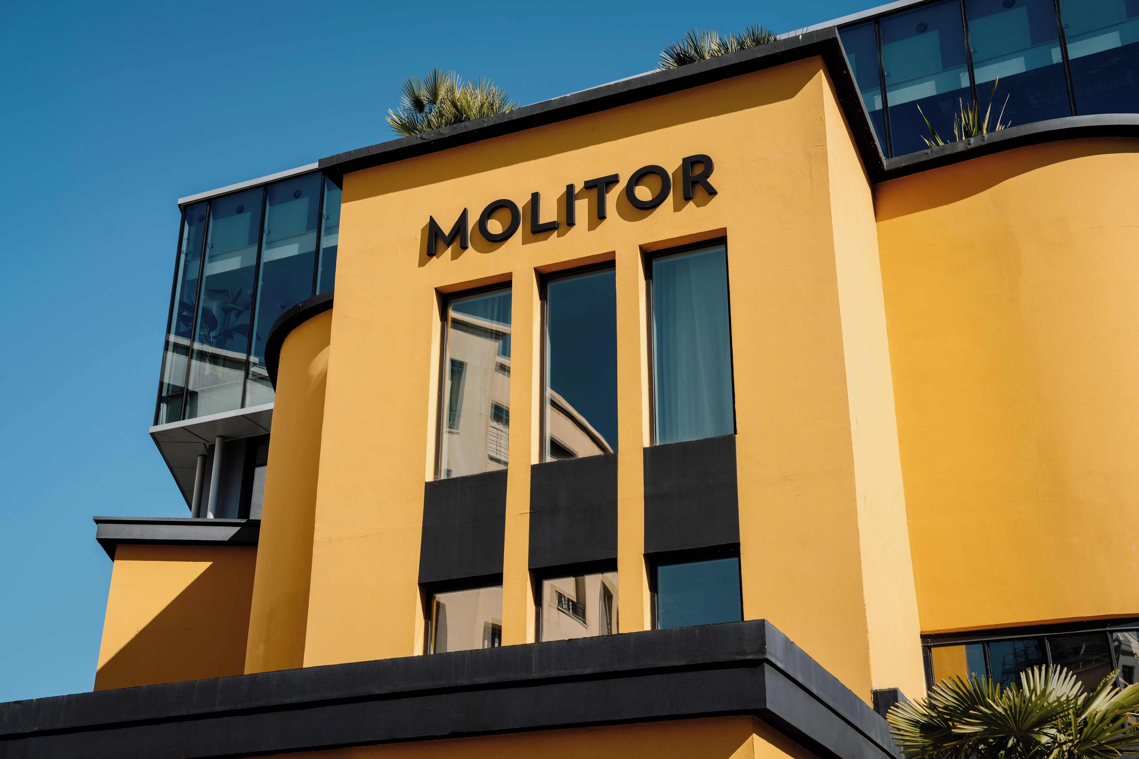 Um edifício com a fachada identificada pela inscrição 'MOLITOR', caracterizado por grandes janelas e um design arquitetônico moderno.