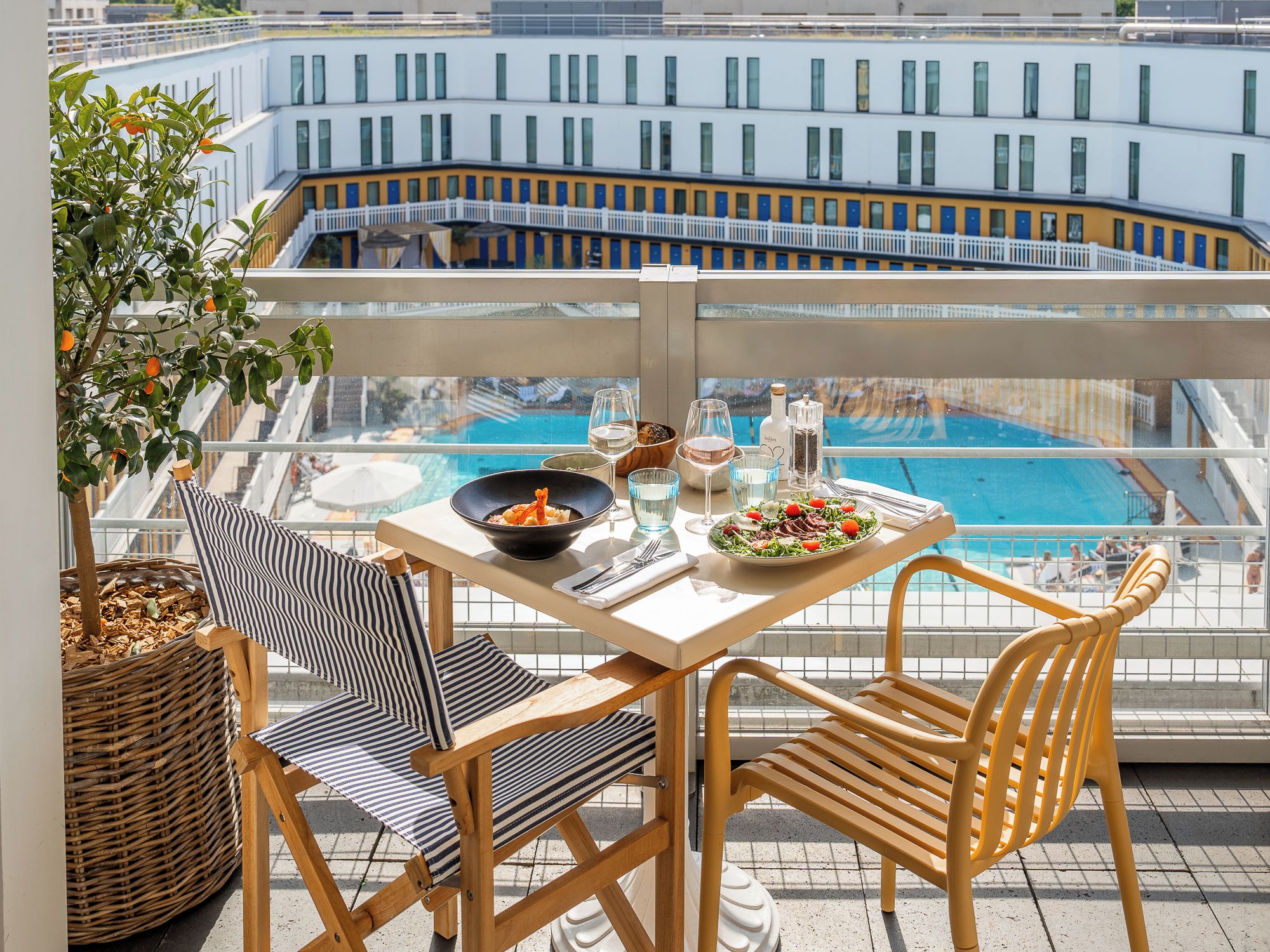 Un tavolo da pranzo con sedie, vista piscina e una pianta su un balcone.
